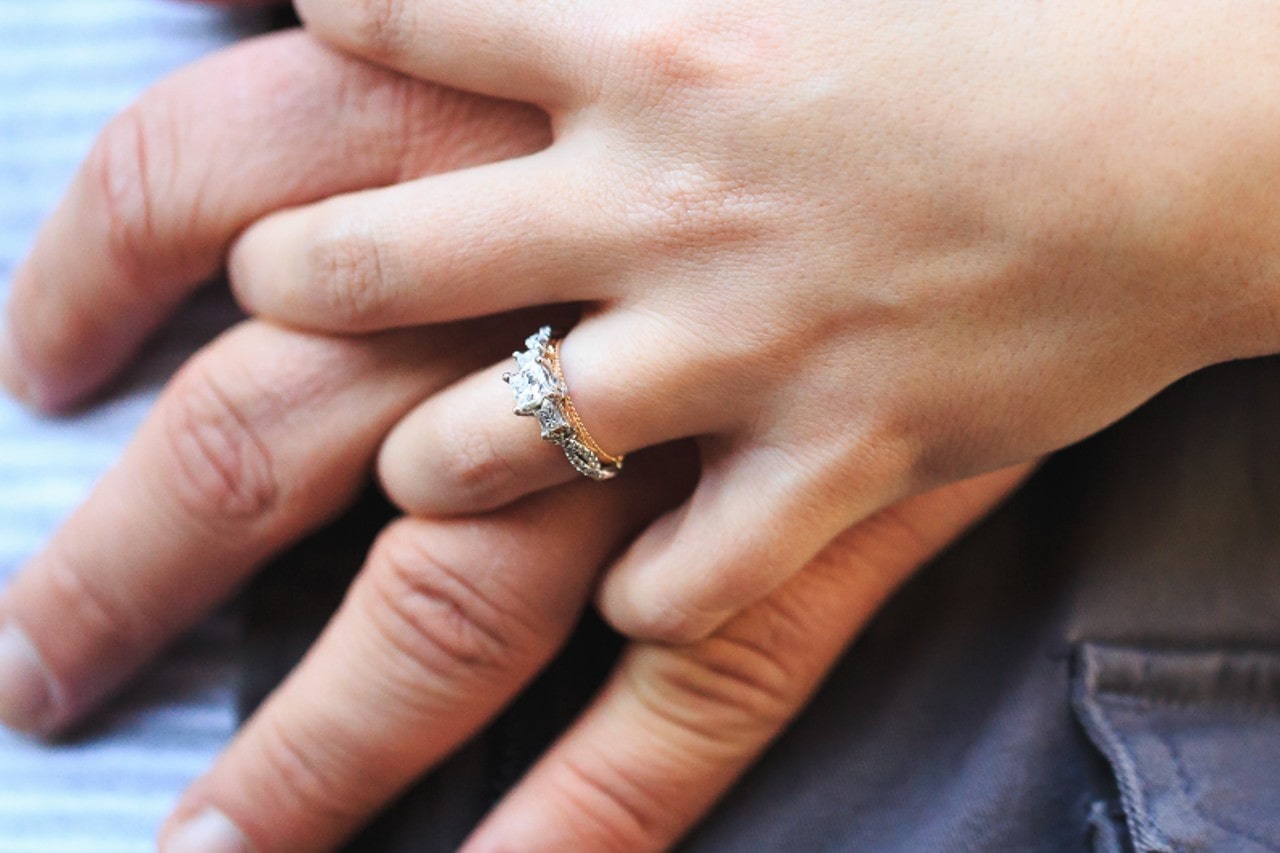 close-up image of hands intertwining, the woman’s hand wearing a vintage-inspired engagement ring
