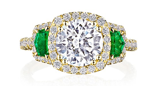 a yellow gold engagement ring featuring a round cut diamond center stone and green sapphire side stones