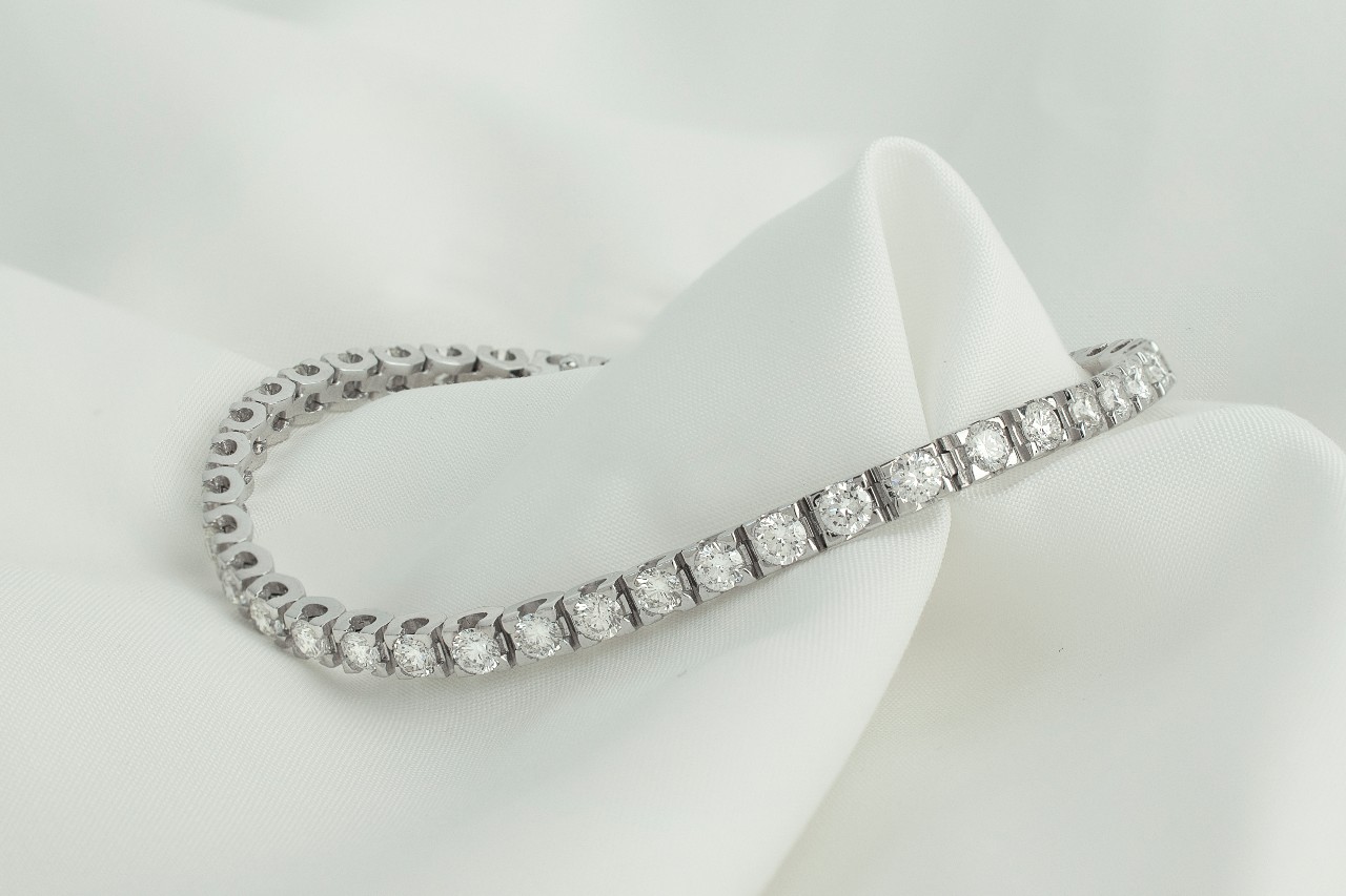 a white gold diamond tennis bracelet lying on a piece of white fabric
