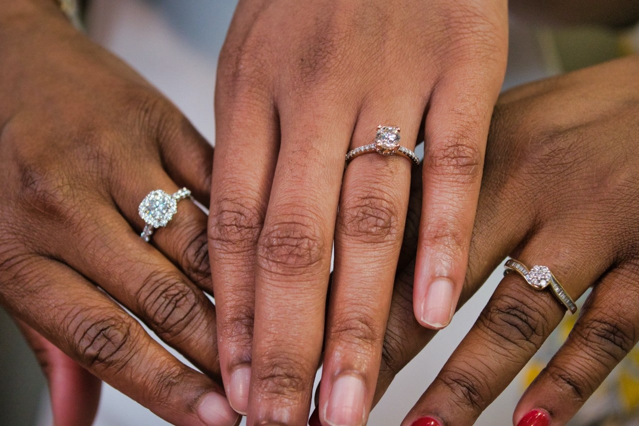 Three women hold their hands out to compare their diamond engagement rings.