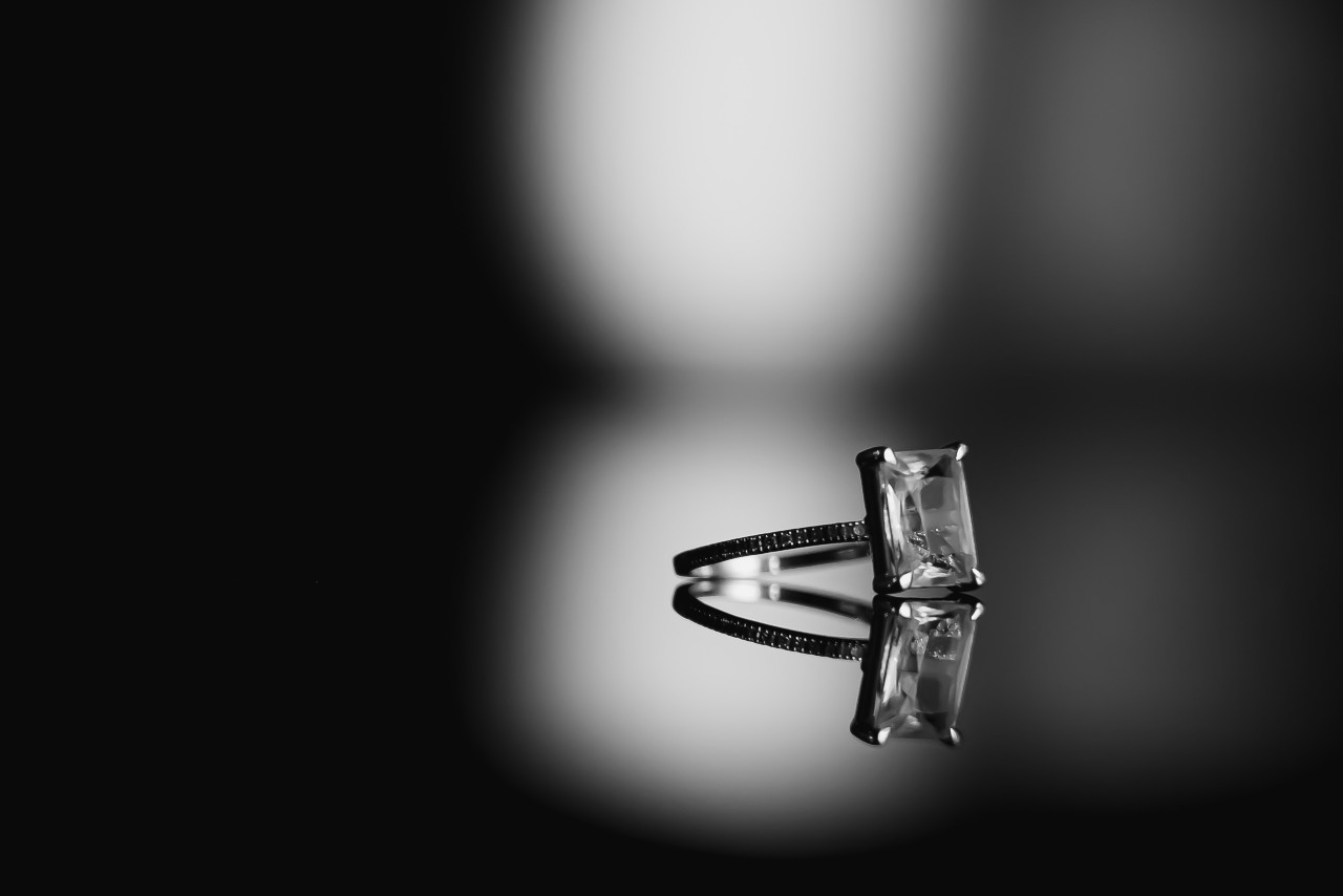 A solitaire emerald-cut diamond ring sits on a reflective surface.