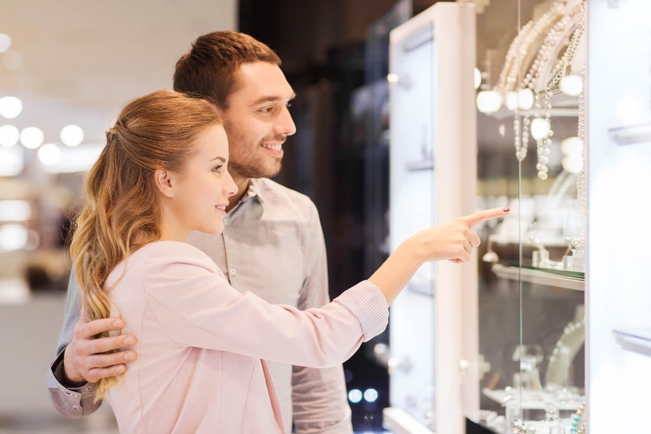 A couple shop for necklaces in a glass case at their local jewelry store. A couple shop for necklaces in a glass case at their local jewelry store.